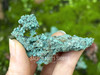 Native copper crystal held between cupped fingers with more copper pieces behind on moss-covered brick, showcasing earthy tones and natural beauty. Native copper crystal held between cupped fingers with more copper pieces behind on moss-covered brick, showcasing earthy tones and natural beauty.