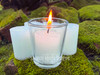several sage bundle handmade votive candles sit on moss covered brick, with one in the foreground in a clear votive cup while lit displaying the candle beauty.