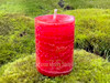 One Dragon's Blood Protection Votive Candle stands on moss covered bricks shown from the front