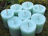 A close up of several Sweetgrass & Cedar Cleansing Votive Candles stand on moss covered bricks shown slighty from above
