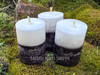 Three Reversing Black and White Votive Candles are shown from the front and slightly above stand on moss covered bricks.
