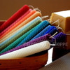 An array of hand-rolled beeswax mini candles in vibrant colors are angled to the side in a basket with a block of beeswax in the background.