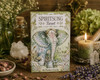 Spiritsong Tarot card deck box featuring an illustrated elephant on the front, styled on a rustic wooden surface with a lit candle, crystals, dried flowers, and greenery.