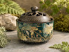 Lotus enamel incense bowl with vented lid displayed outdoors among moss and natural stone in bright sunlight.