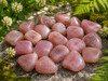 Collection of polished Natural Strawberry Quartz tumbled stones displaying soft pink hues in a natural outdoor setting.
