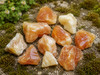 Close-up of Natural Honey Calcite rough stones arranged on a rustic stone surface with moss, emphasizing their rich honey-gold hues, natural crystal formations, and unique mineral variations.