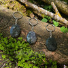 Three polished Moss Agate worry stone keychains resting on a woodland log in sunlight, showing the unique natural colors, inclusions, and patterns of each stone.
