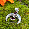 Close view of sterling silver moon pendant with round faceted Garnet above a hanging deep red faceted Garnet.