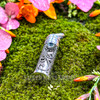 Sterling silver intention and prayer bottle pendant with ornate scrollwork and faceted Blue Topaz displayed on green moss with colorful flowers.