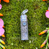 Blue Topaz sterling silver intention vial pendant showing faceted gemstone, ornate raised scrollwork, cylindrical cap and pendant bail.