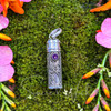 Sterling silver Amethyst intention and prayer bottle pendant resting on green moss with pink and orange flowers.