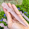 Rose Quartz crystal athame held in hand to show its size, polished finish, carved blade, crossguard, and star-shaped handle.