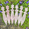 Six Rose Quartz crystal ritual athames displayed together on lush green groundcover with purple flowers.