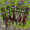 Six Mahogany Obsidian crystal athames with star-shaped handles arranged on green groundcover with small purple flowers.