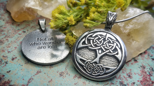 Two celtic tree of life pendant necklaces rest on natural crystals-steel snake change shown is not included. One shows the front design, and the other shows the inscription on the back: Not all who wander are lost.