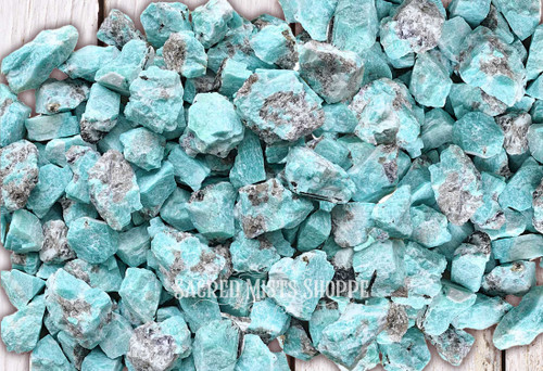 an assortment of natural amazonite crystal gemstones in their natural state lie on a light colored table.