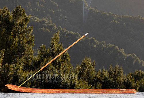 Woods Premium Masala Incense Stick burning on a wood ash catcher sitting on a stone ledge with trees in the background.