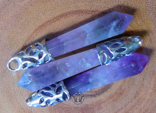Three amethyst crystal point pendant lying on a wood slice.