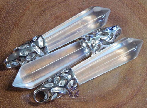 Three quartz crystal point pendants lying on a wood slice.
