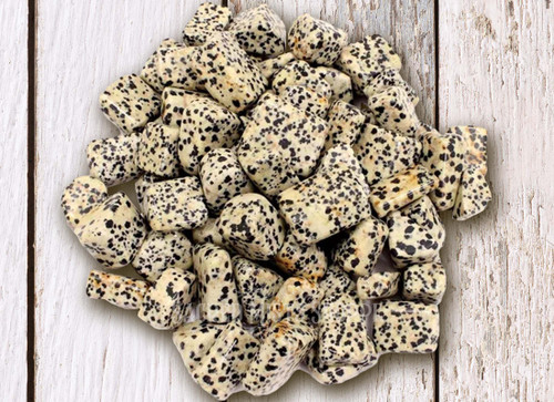 Dalmatian Jasper lies on a distressed light wood table. It is excellent for joy, peace, playfulness, grounding, and family.