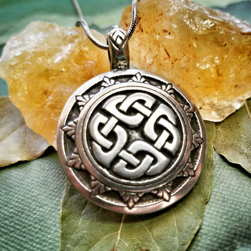 One knotted shield pendant necklace lying on a green altar cloth with dried leaves and natural citrine chunks.
