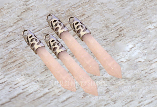 Four rose quartz crystal pendant points with ornate silver bail are lying on a light-colored distressed wood table.