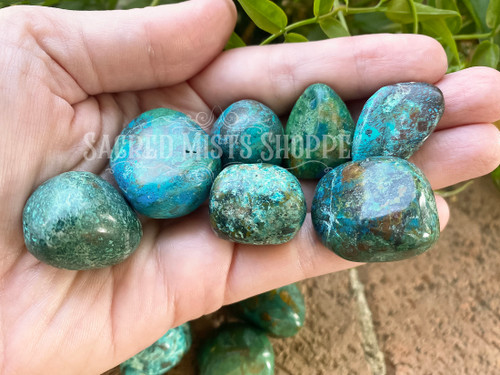 several tumbled crysocolla stones lie on an open palm showing variations in color, size, and markings.
