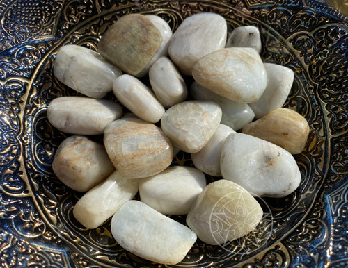 A close-up of tumbled hiddenite crystals in a large metal bowl glistening in the sunlight; natural green hiddenite for heart chakra healing, emotional balance, and love energy; sunlit hiddenite gemstones for gratitude, joy, and releasing past trauma; high-vibration hiddenite for crystal healing, meditation, and reiki; rare green hiddenite tumbled stones for inner peace, relationship harmony, and spiritual growth.