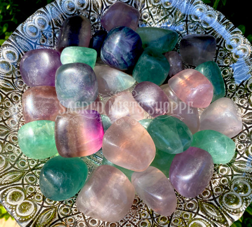an assortment of tumbled extra large rainbow fluorite crystals are in a large silver bowl in filtered sunlight.