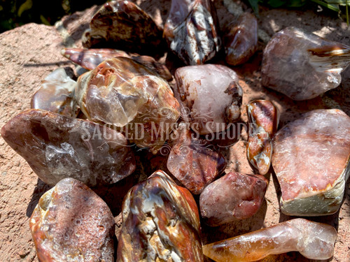 Several amphibole angel phantom quartz crystal stones lie on brickwork in filtered sunlight.