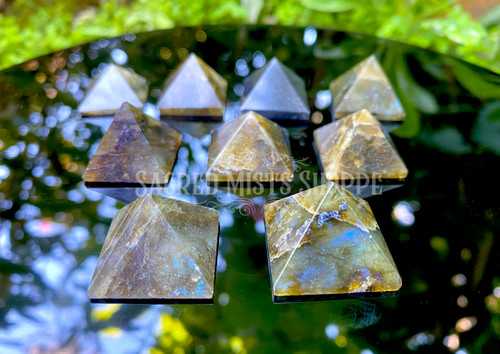 several petite labradorite crystal pyramids rest on a black obsidian mirror showcasing variation in size, markings, and flash.
