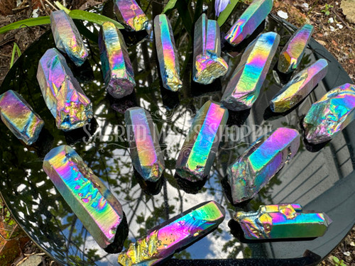several rainbow flame aura crystal points lie on a black obsidian crystal mirror showing variation in color, size, and shape.