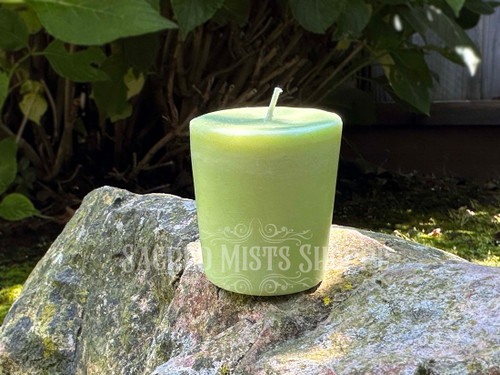 one banishing votive candle standing on a rock in filtered sunlight with greenery in the background