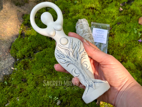 natures spiral goddess statue held in a hand to show size with a smudge bundle and ritual-sized incense stick in the background.
