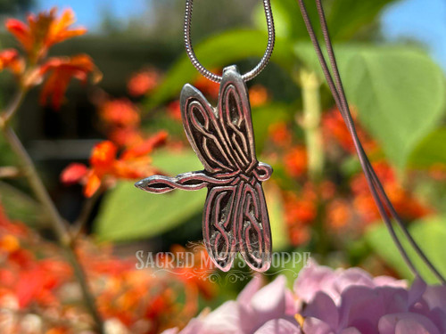 Celtic knot dragonfly pendant cast in pewter and made the USA hanging on a stainless steel snake chain hanging in front of a floral backdrop/