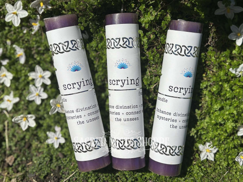 Three Scrying Purple Pillar Candles fanned out and lying on a bed of greenery with white flowers. The candle fragrance is frankincense, made with pure essential oil. Perfect for divination, scrying, visions.