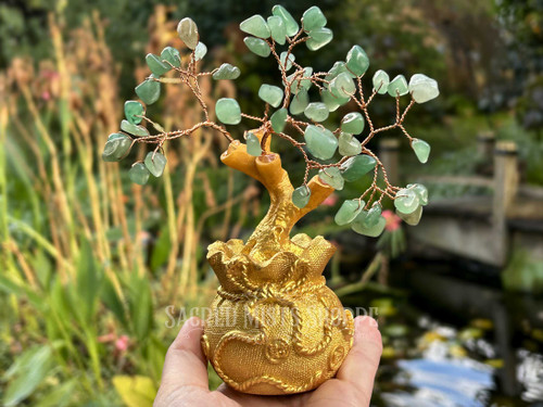 One jade gemstone money tree being held in a hand with a koi pond in the background. These are perfect for Attract Wealth, Growth, Abundance, Good Luck, Prosperity, Harmony, Good Fortune, Money Spells, Attract Money