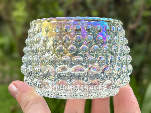 One iridescent glass candle holder with a hobnail design is held between fingers to show the size and iridescence.