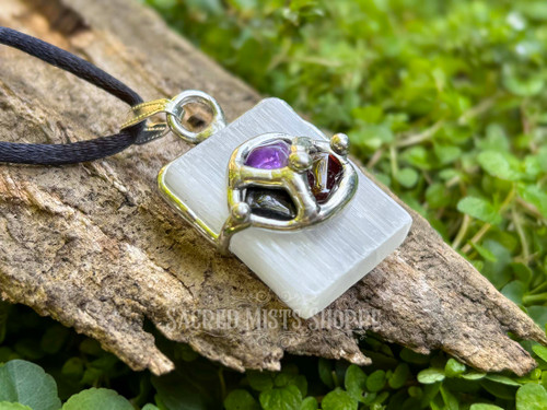 one selenite spiritual gemstone pendant necklace with amethyst, garnet, and hypersthene showing one stone layout lying on a piece of wood surrounded by greenery. Perfect for seeking clarity, energy clearing, empowerment, and clearing blockages.