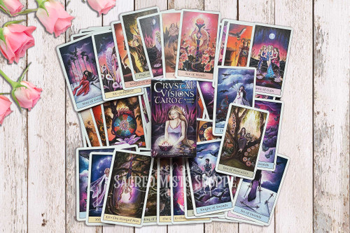 Crystal Visions Tarot Deck by Jennifer Galasso rests on a light-colored idstressed table with the cards spread out underneath the box and pink roses in the upper left corner.