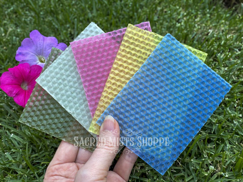 five sheets of color magick beeswax fanned to show colors included held in a hand with grass and flowers in the background. each kit comes with one precut beeswax sheet in blue, yellow, pink, white, and green. these are perfect for making your own spell and ritual candles.