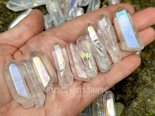 several angel or opal aura quartz points lie on an open palm, displaying variations in the stones, there are more stones in the background