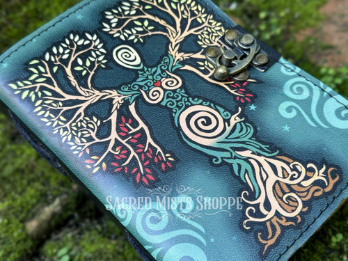 Close-up overhead shot of a green leather Goddess journal angled to the left on moss-covered brick, highlighting the embossed design.