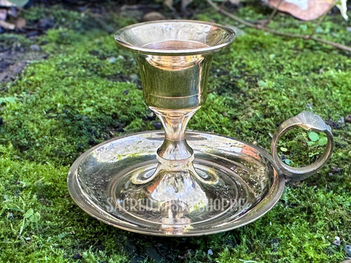 close up of one brass chamberstick old worlde candle holder on a bed of greenery shown from the front