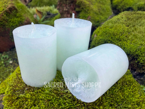 three sage bundle handmade votive candles sit on moss covered brick, with one in the foreground lying on its side.