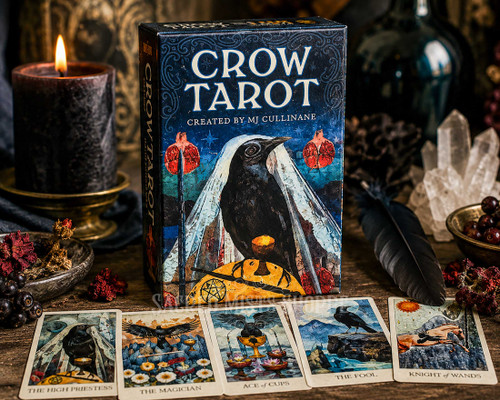 Crow Tarot deck shown from the front with several cards fanned in the front of the box surrounded by crystals and candlelight