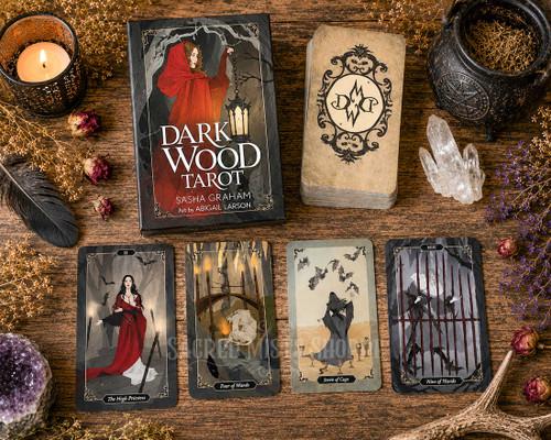 Top-down view Dark Wood Tarot deck displayed with cards, crystals, natural elements on a rustic wooden tabletop illuminated by warm candlelight.