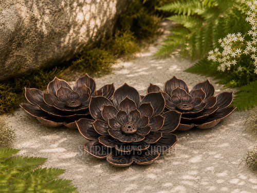Three copper lotus incense burners arranged together on natural stone in a sunlit garden surrounded by moss, ferns, and delicate white flowers.