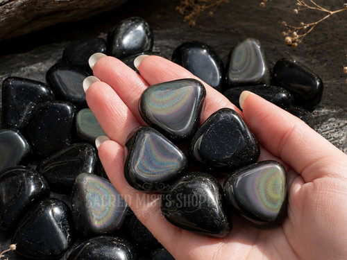 Hand holding polished Rainbow Obsidian tumbled stones highlighting glossy black surfaces and colorful rainbow sheen.