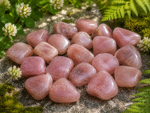 Collection of polished Natural Strawberry Quartz tumbled stones displaying soft pink hues in a natural outdoor setting.
